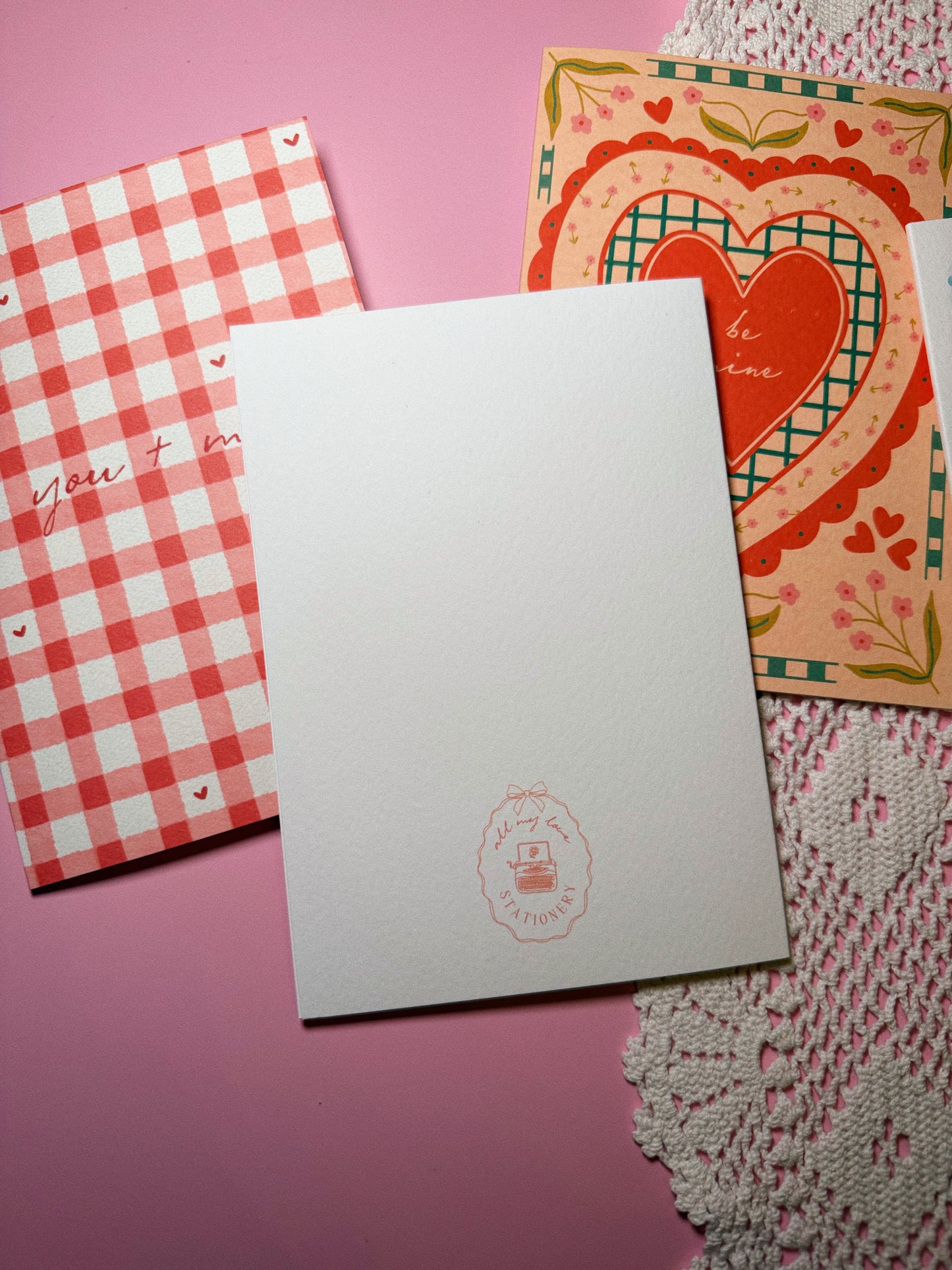Three greeting cards with one flipped over showing the white background and pink logo of all my love stationery
