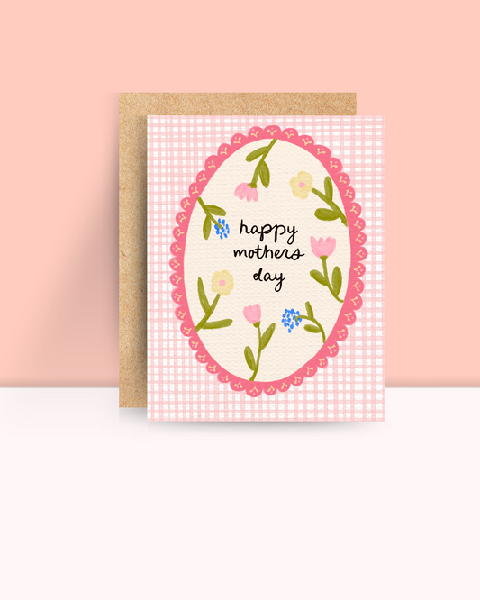 A pink gingham card with a delicate embroidery style hoop with the words happy mother's day on it surrounded by flowers